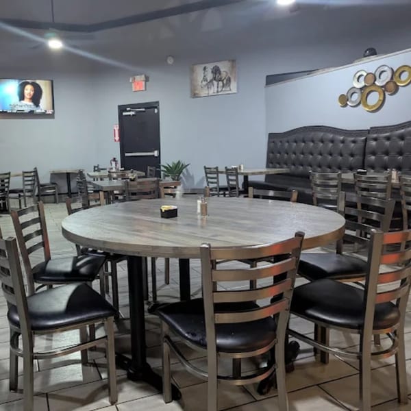 A restaurant interior with round wooden tables, metal chairs, and a long black booth against a gray wall.