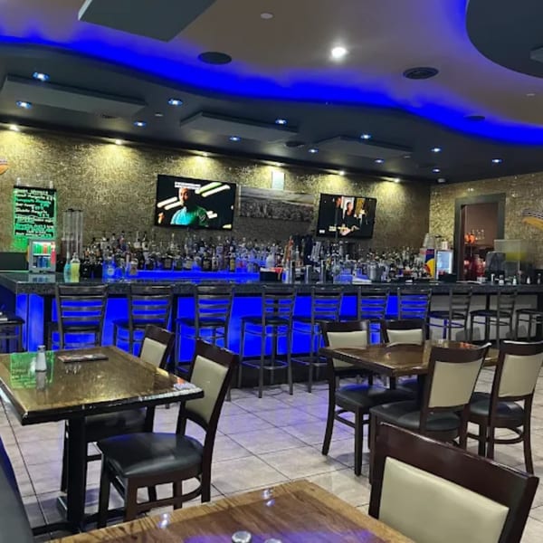 A restaurant interior with a long bar illuminated by blue lights and several dining tables.
